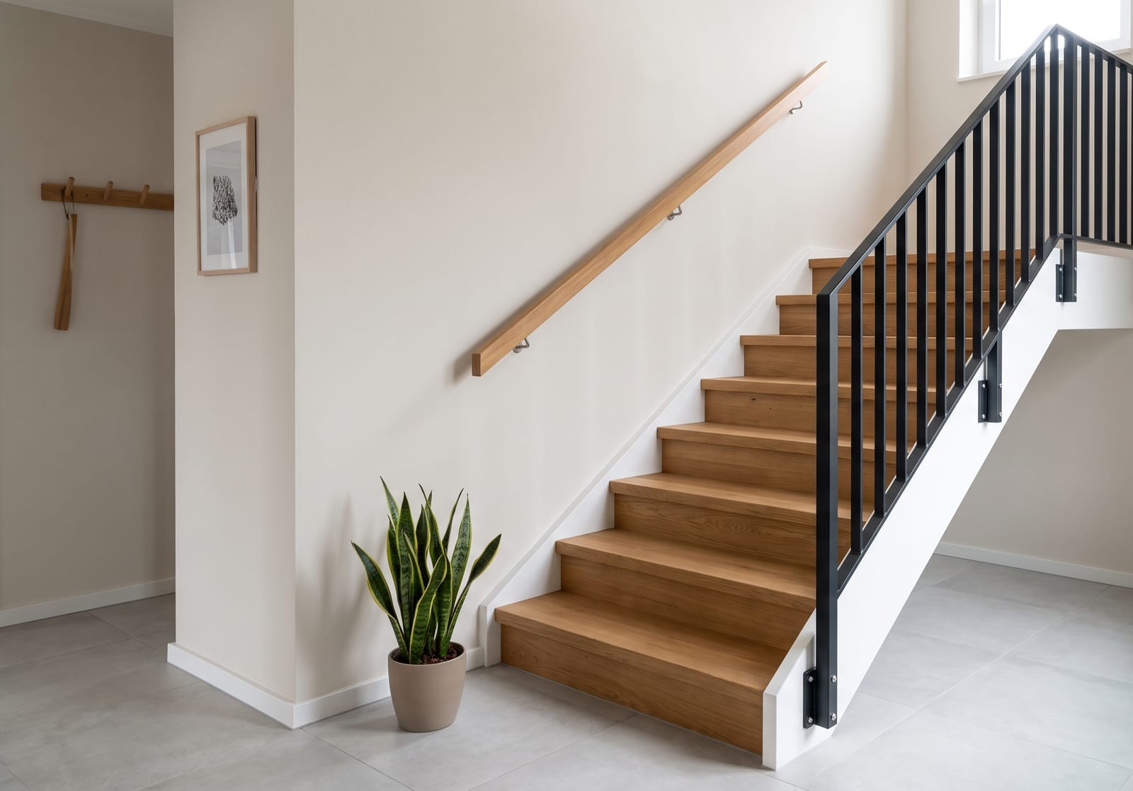 Gerade Treppe mit renovierten Eichenstufen, Handlauf an der Wand und schwarzem Stahlgel&auml;nder